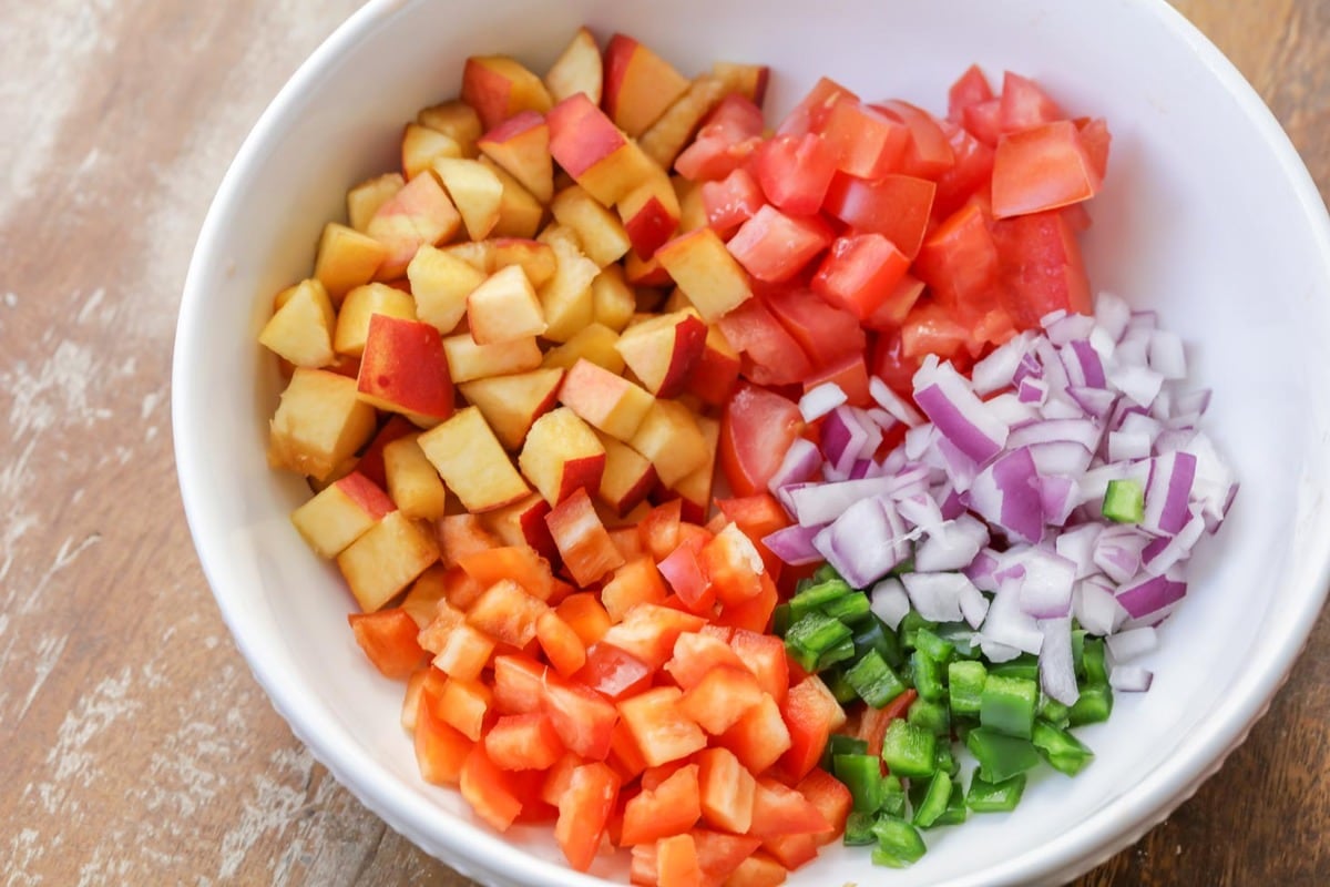 Cut peaches and veggies in a white bowl.