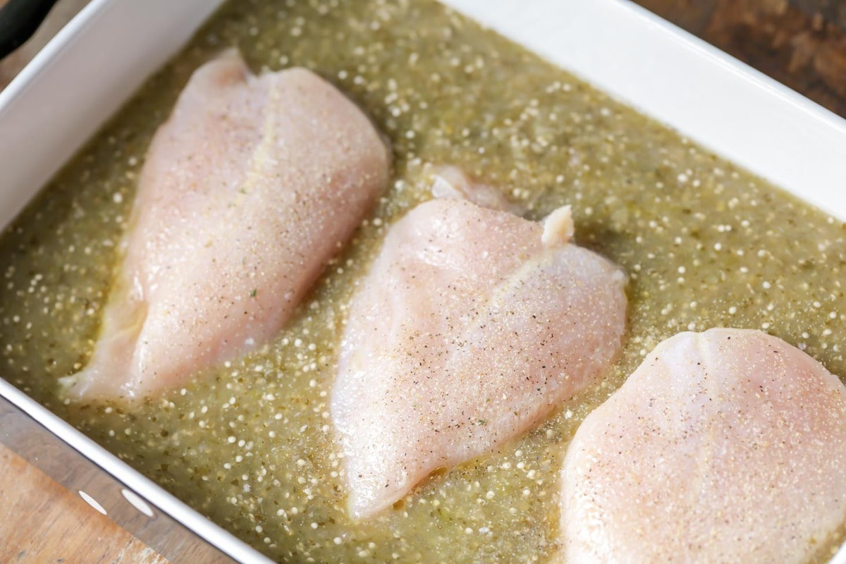 Chicken breasts in green salsa in a baking dish for salsa verde chicken.