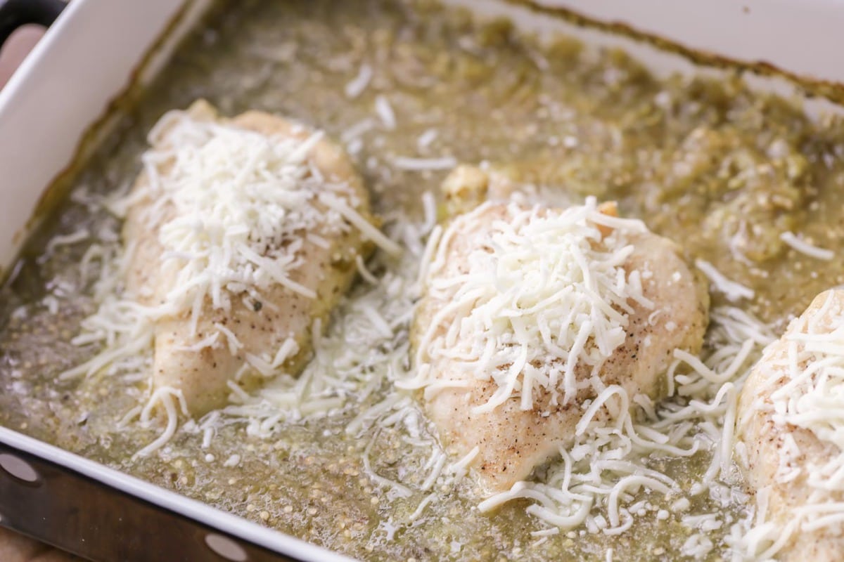 Salsa verde chicken topped with shredded cheese in a baking dish.