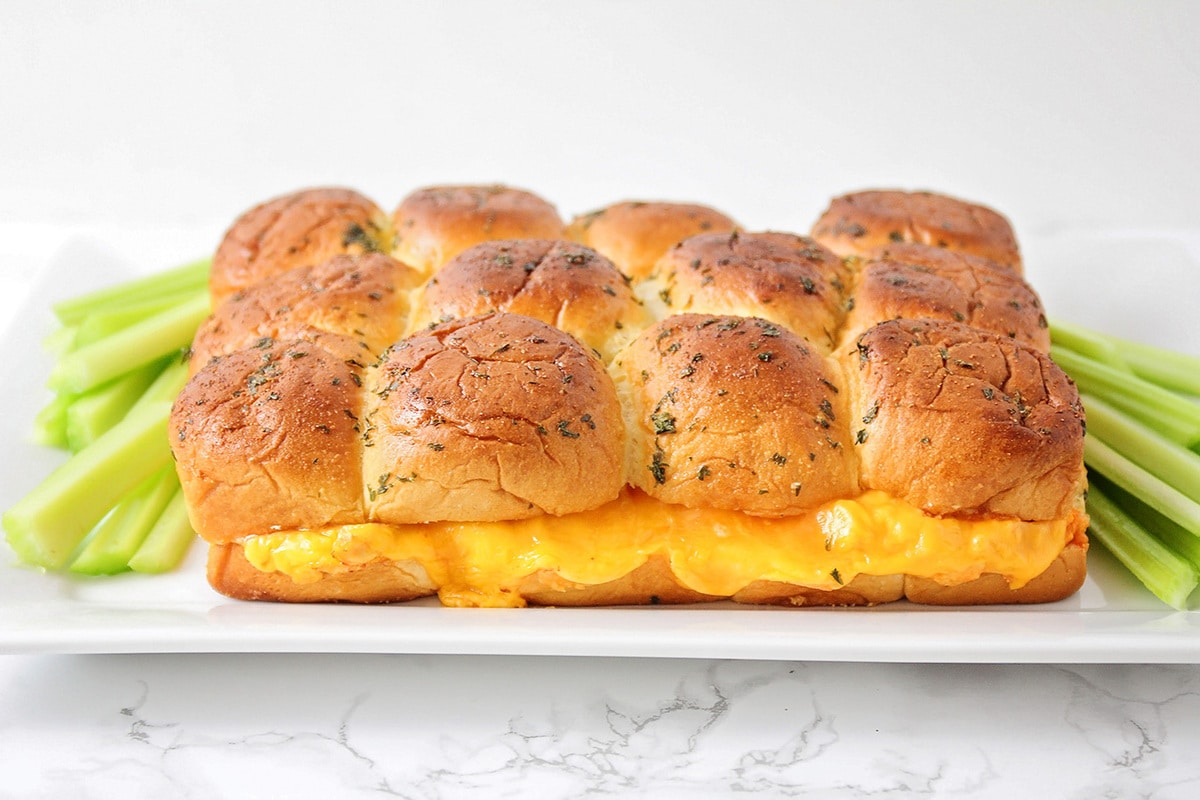 Buffalo chicken sliders with a side of celery sticks on a white platter. 