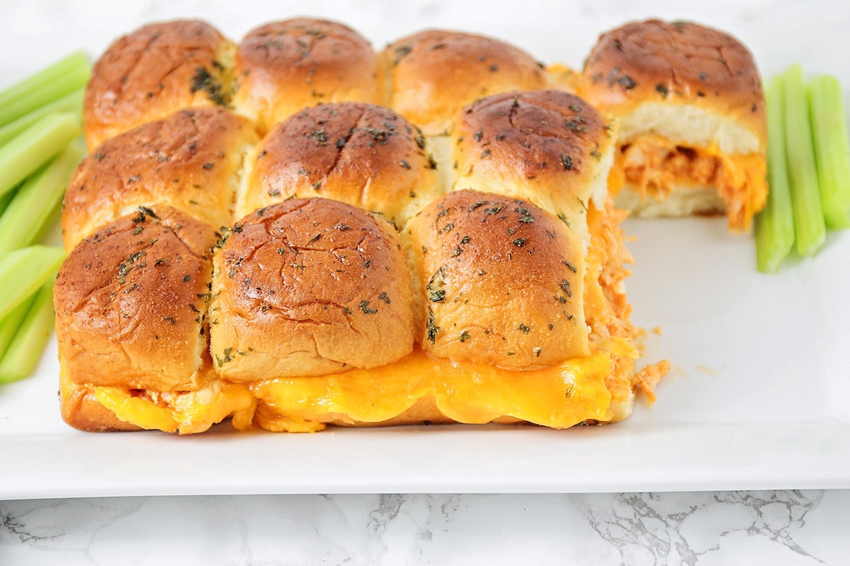 Cheesy Buffalo chicken sliders on plate with celery, with two missing.