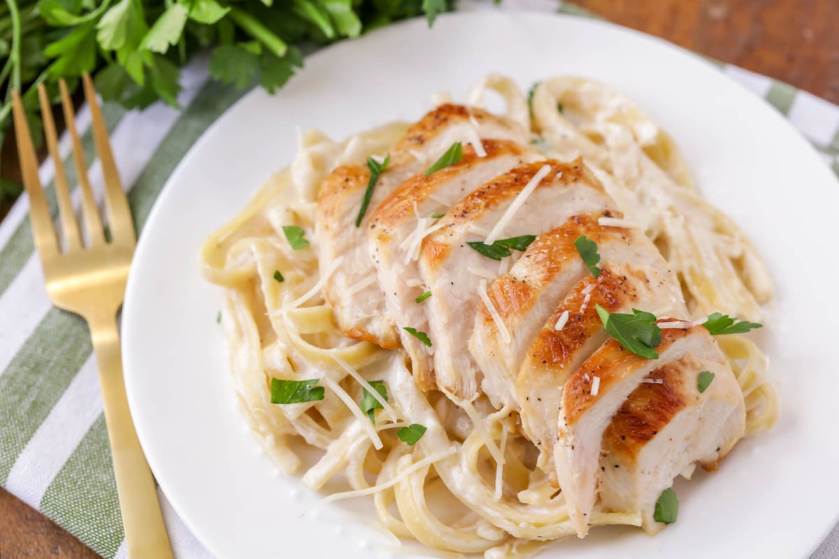 Go-to chicken pasta recipes including chicken alfredo close up on a white plate.