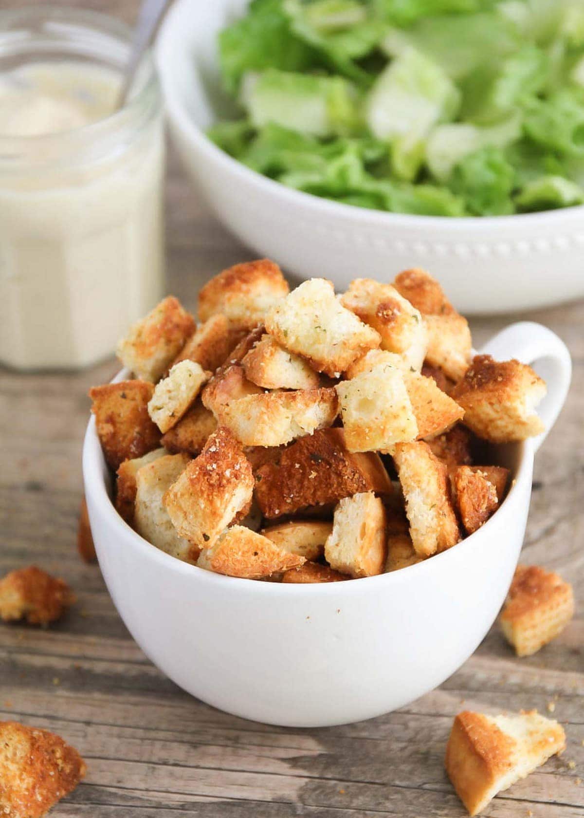 Homemade Croutons served in a white bowl next to a salad.