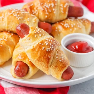 Easy pigs in a blanket stacked on each other on white plate.