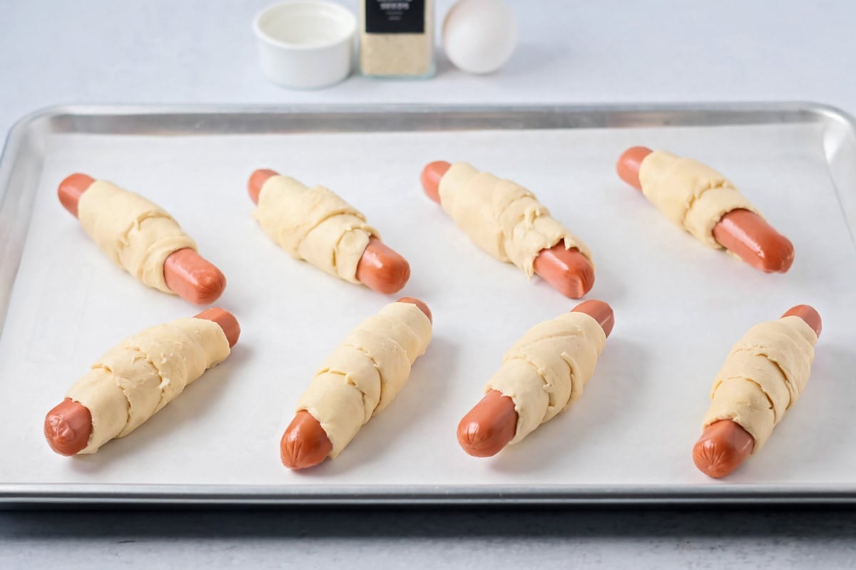 Crescent dough wrapped hot dogs on baking sheet.