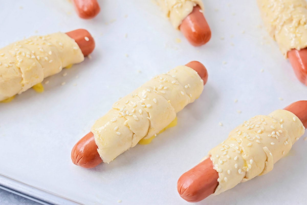 Egg wash and sesame seeds sprinkled on Pigs in Blanket.