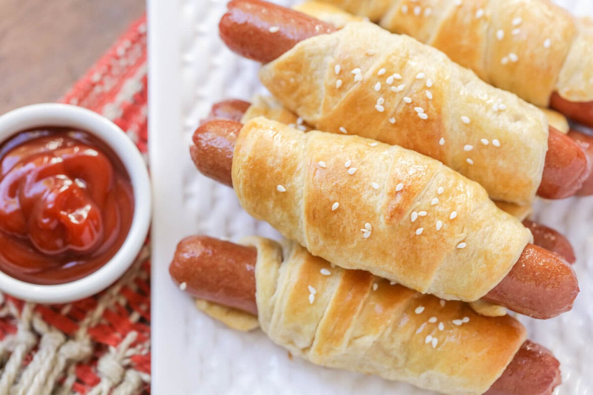 Pigs in a Blanket on white dish served with a side of ketchup.