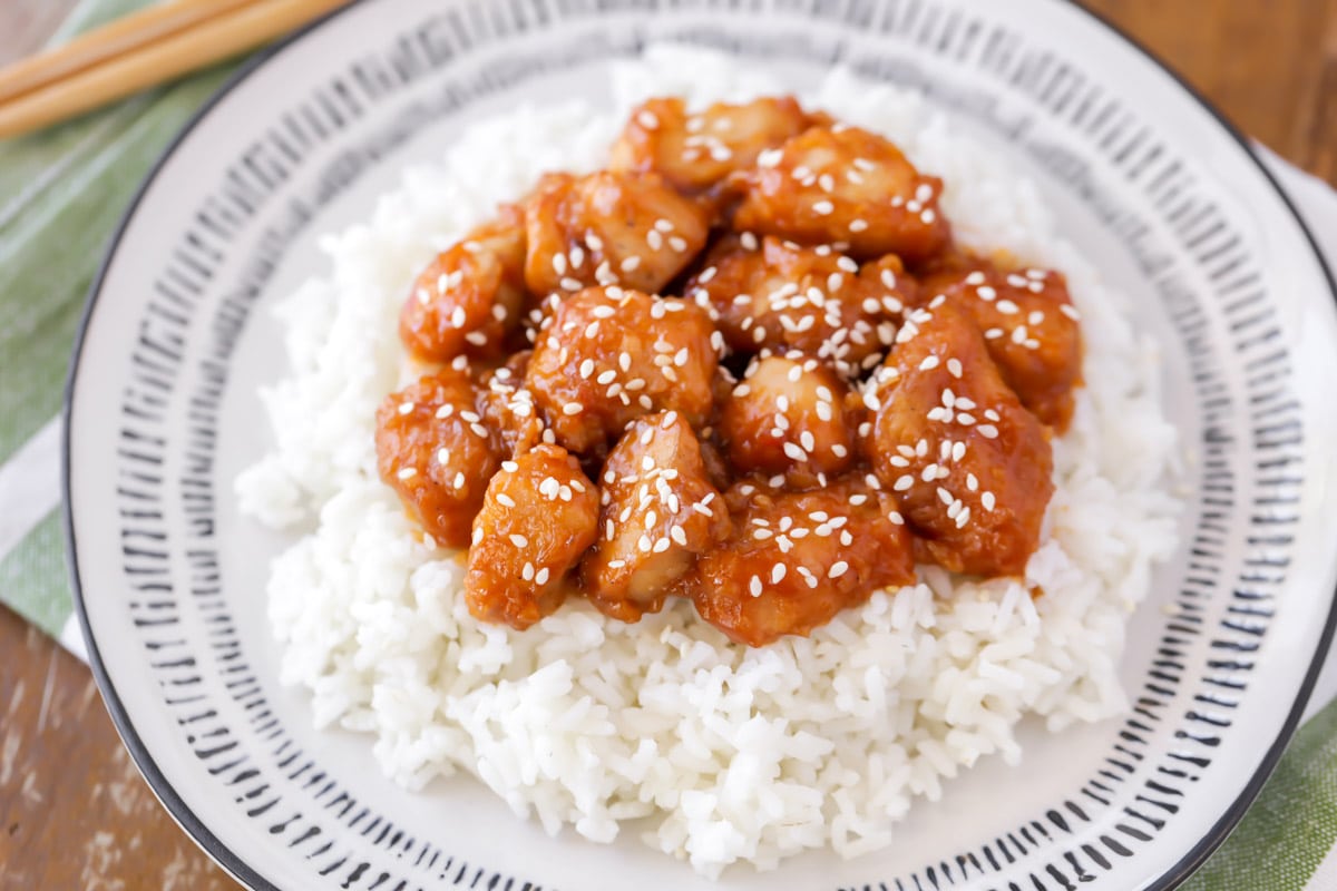 Asian Dinner Recipes - Sesame chicken on top of white rice on a white plate. 