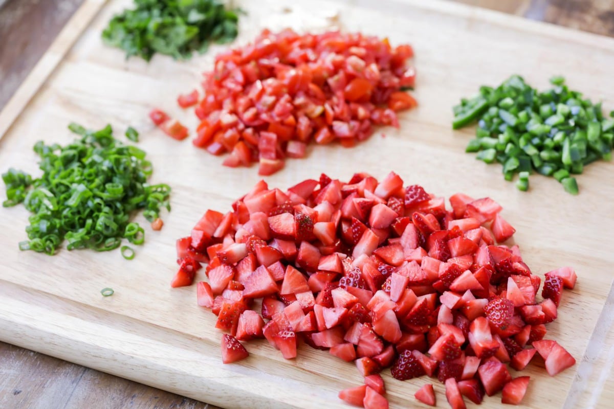 Chopped strawberries, jalapenos, and herbs on a cutting board.