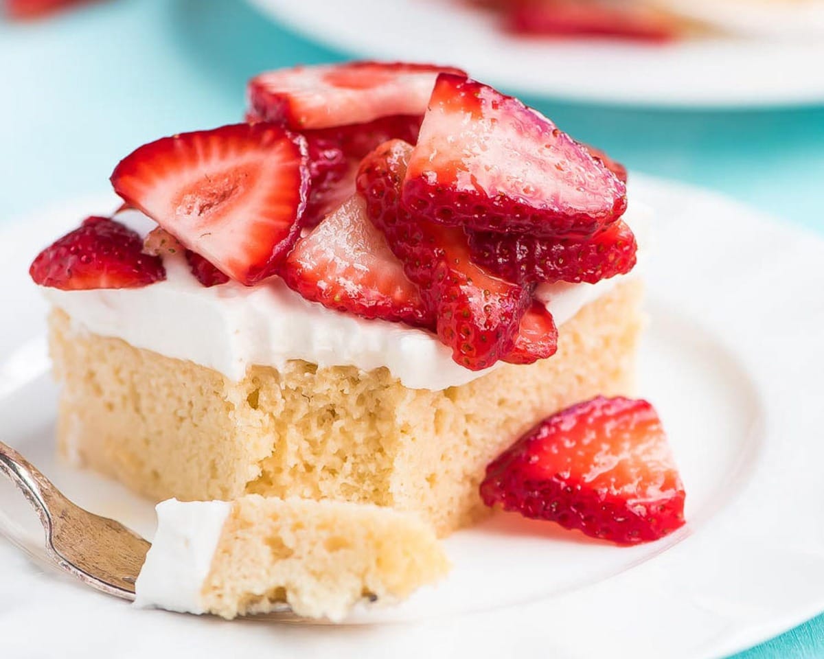 Valentine's Day Desserts - Tres Leches Cake topped with sliced strawberries on a white plate. 