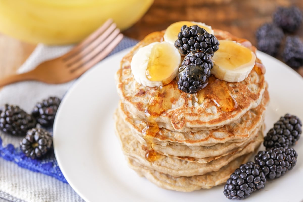 A stack of banana oatmeal pancakes topped with blackberries and syrup.
