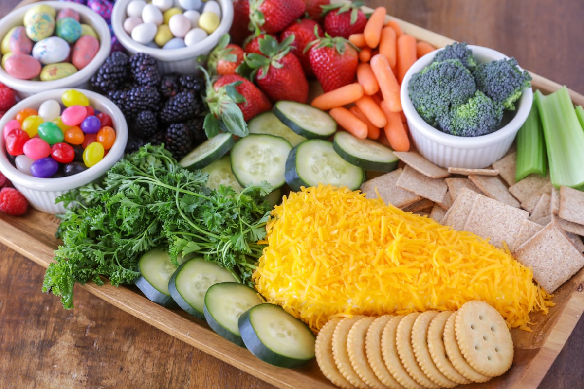 Easter charcuterie board with fresh veggies, fresh fruit, crackers, cheese dip and various Easter candies.