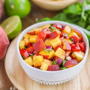 Easy peach salsa recipe in white bowl with ingredients scattered around.