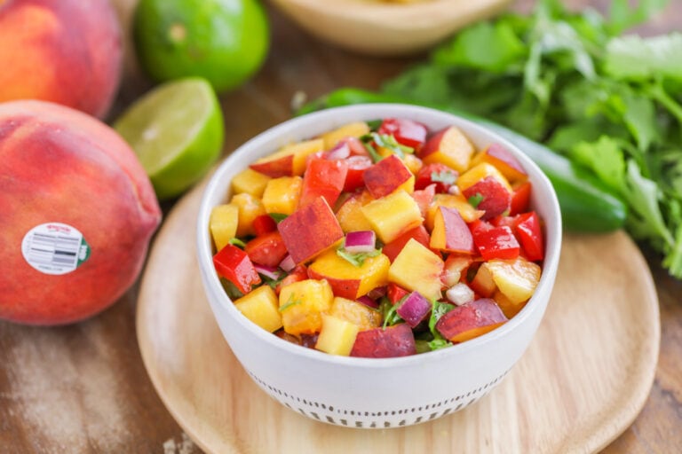 Easy peach salsa recipe in white bowl with ingredients scattered around.