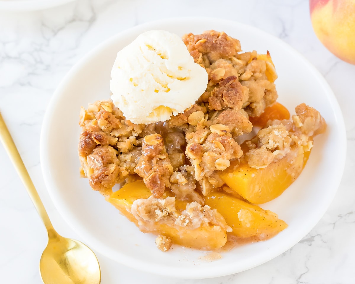 A bowl of peach crisp with vanilla ice cream in a white bowl. 