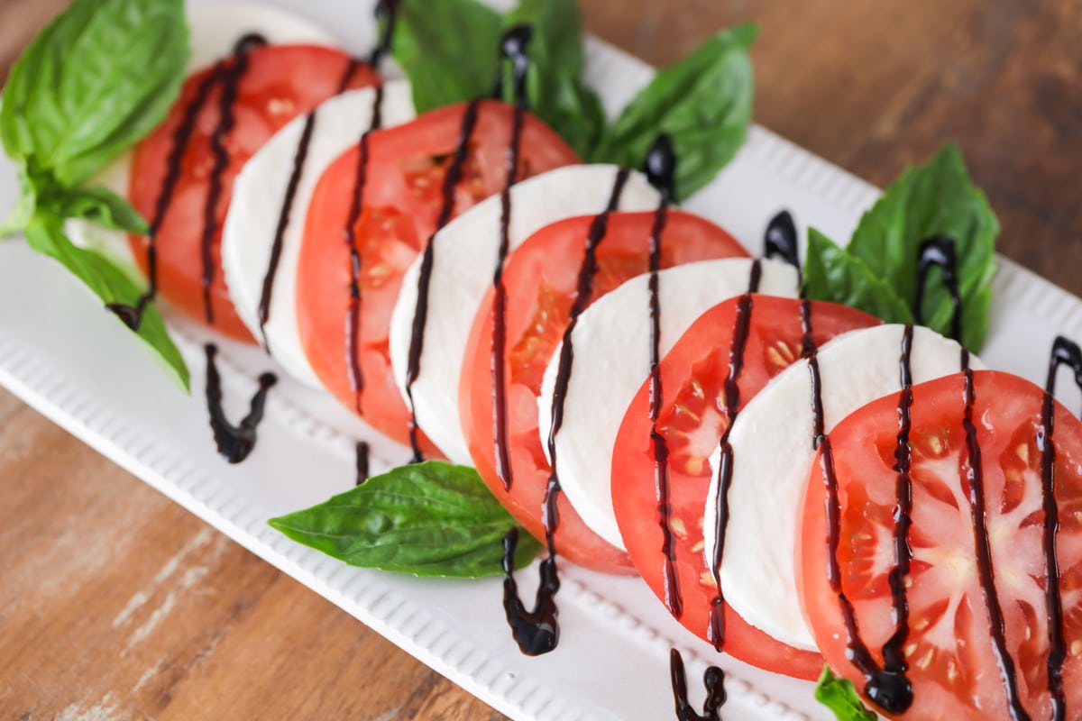 Tomato mozzarella salad on a platter with fresh basil and balsamic glaze.