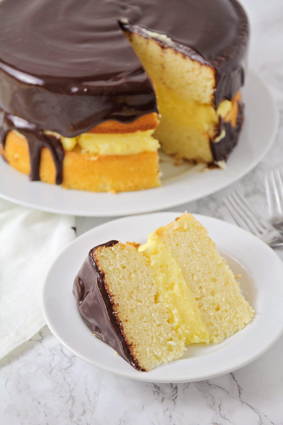 Boston cream pie slice on a white plate.