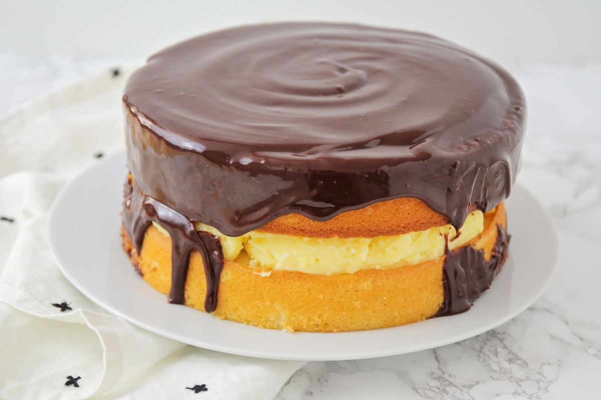 Cake topped with chocolate ganache on a white platter.