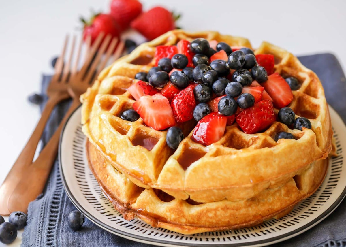 Two buttermilk waffles stacked on a blue and white plate topped with fresh berries and syrup. 