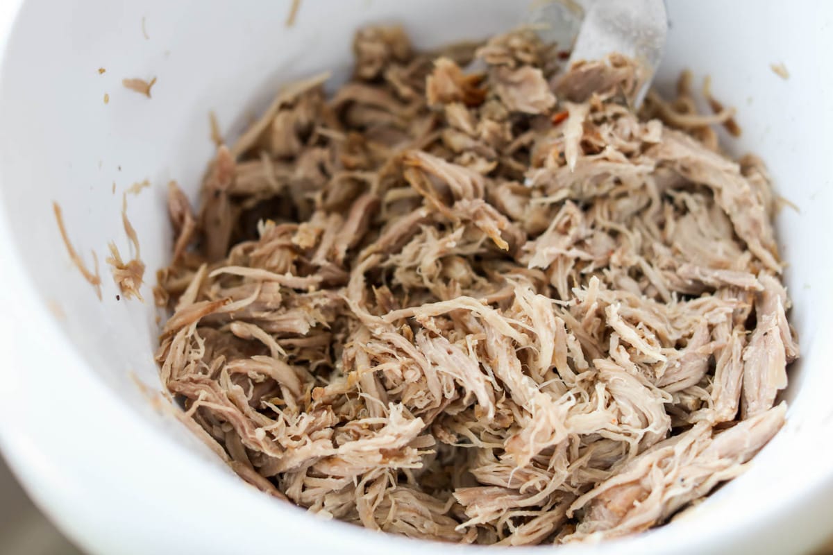 Shredded Kalua Pork in slow cooker with two forks for shredding.