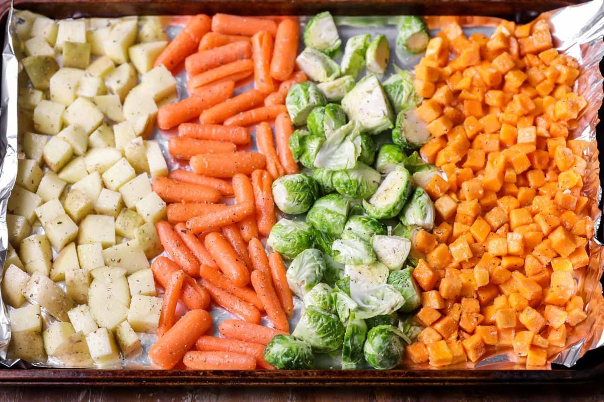 Uncooked diced potatoes, baby carrots, diced Brussel sprouts and diced sweet potatoes on a foil lined baking sheet. 