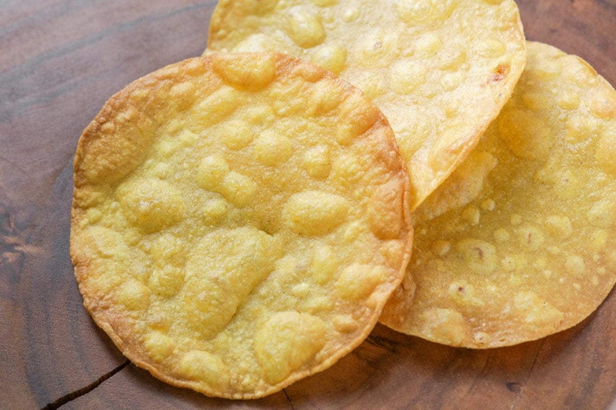 Stack of fried corn tortillas on a wooden table.