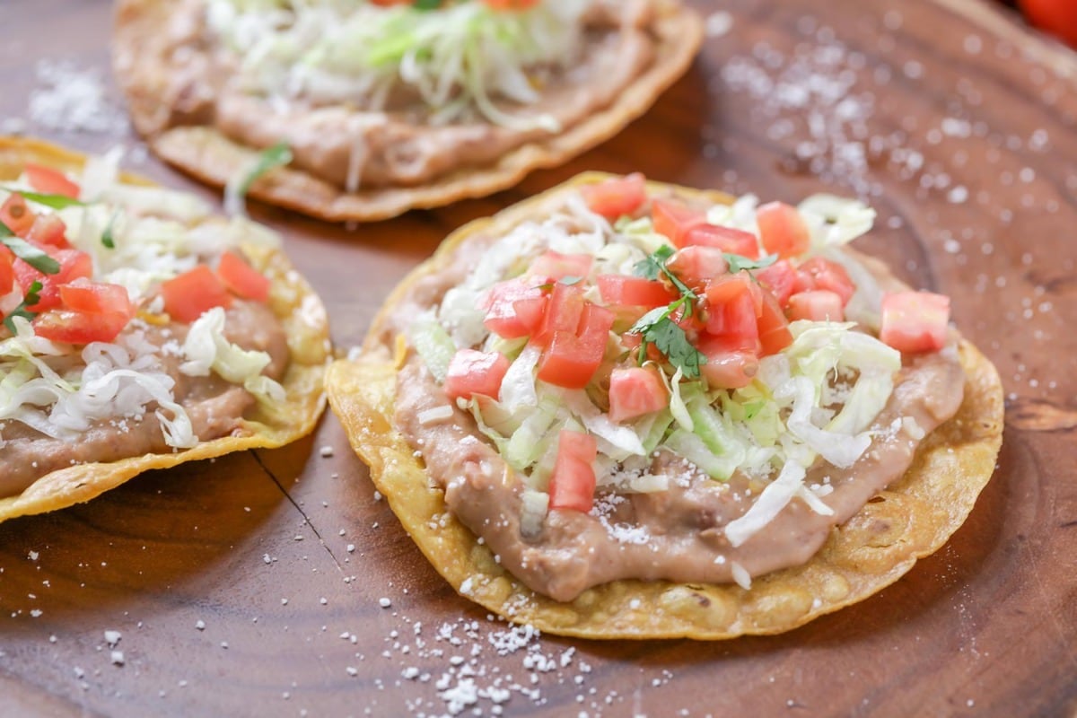 Three tostadas topped with refried beans, shredded lettuce, tomatoes, and cheese