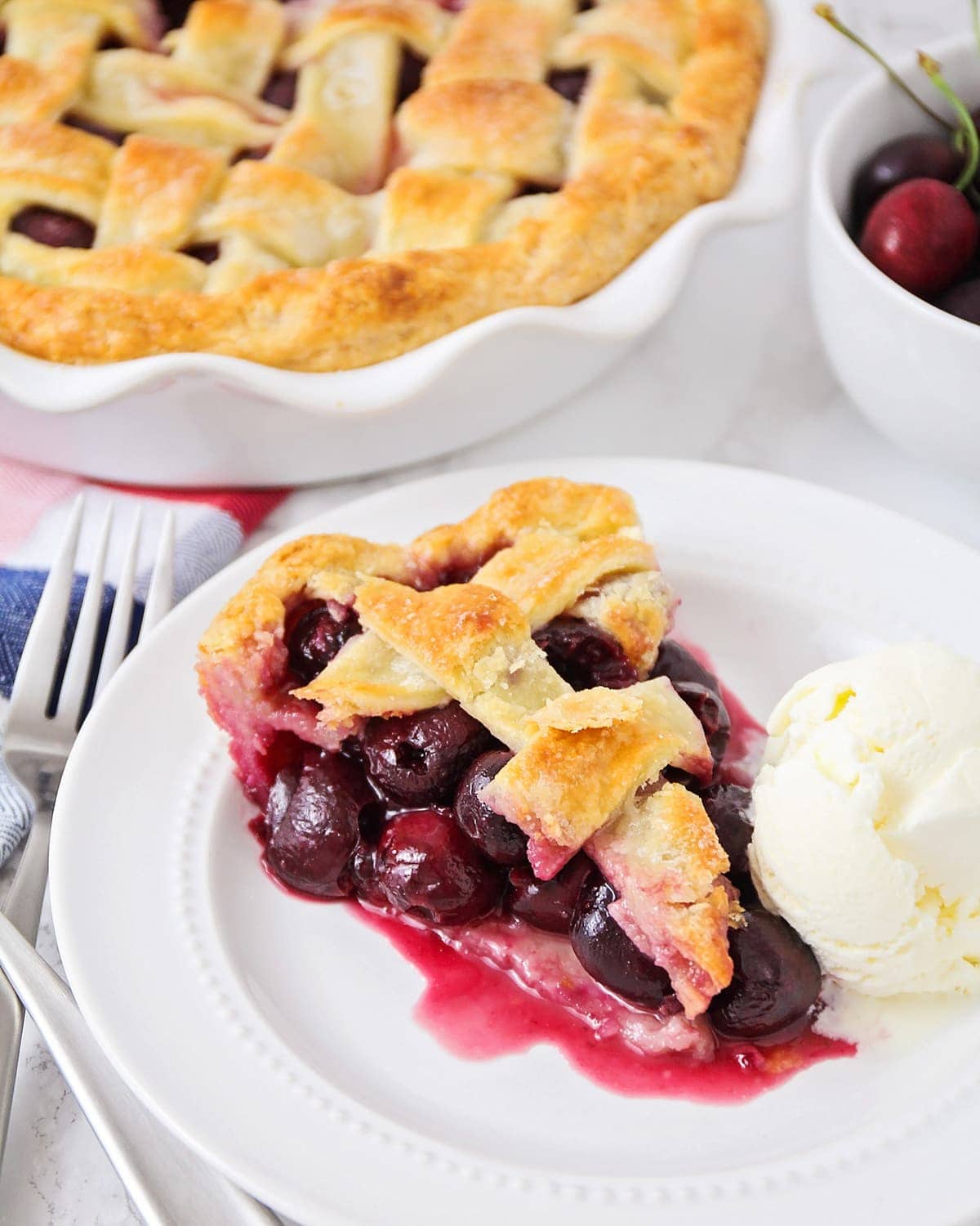 Cherry pie slice on plate served with ice cream.