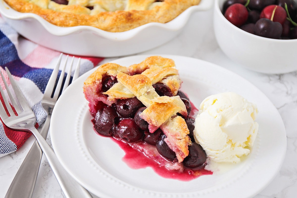 A slice of cherry pie with a scoop of vanilla ice cream on a plate.