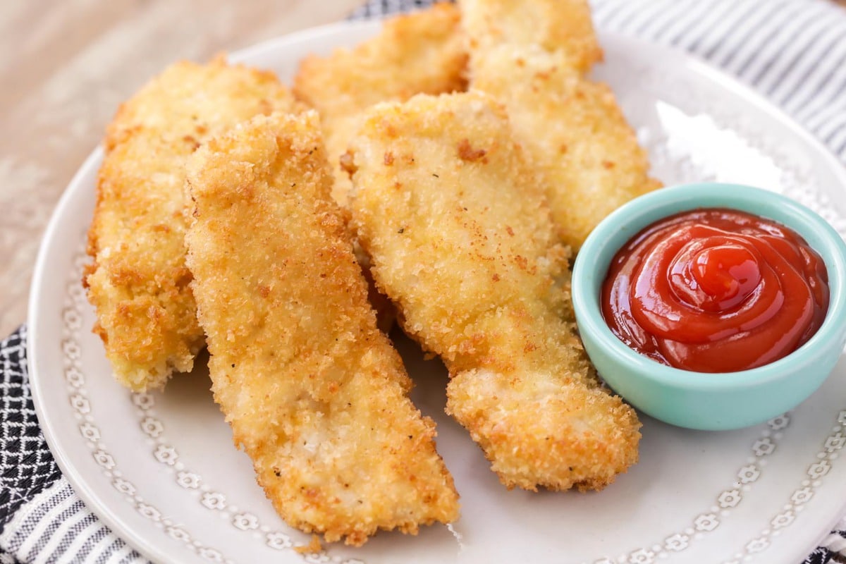 Chicken strips on a plate with a side of ketchup.