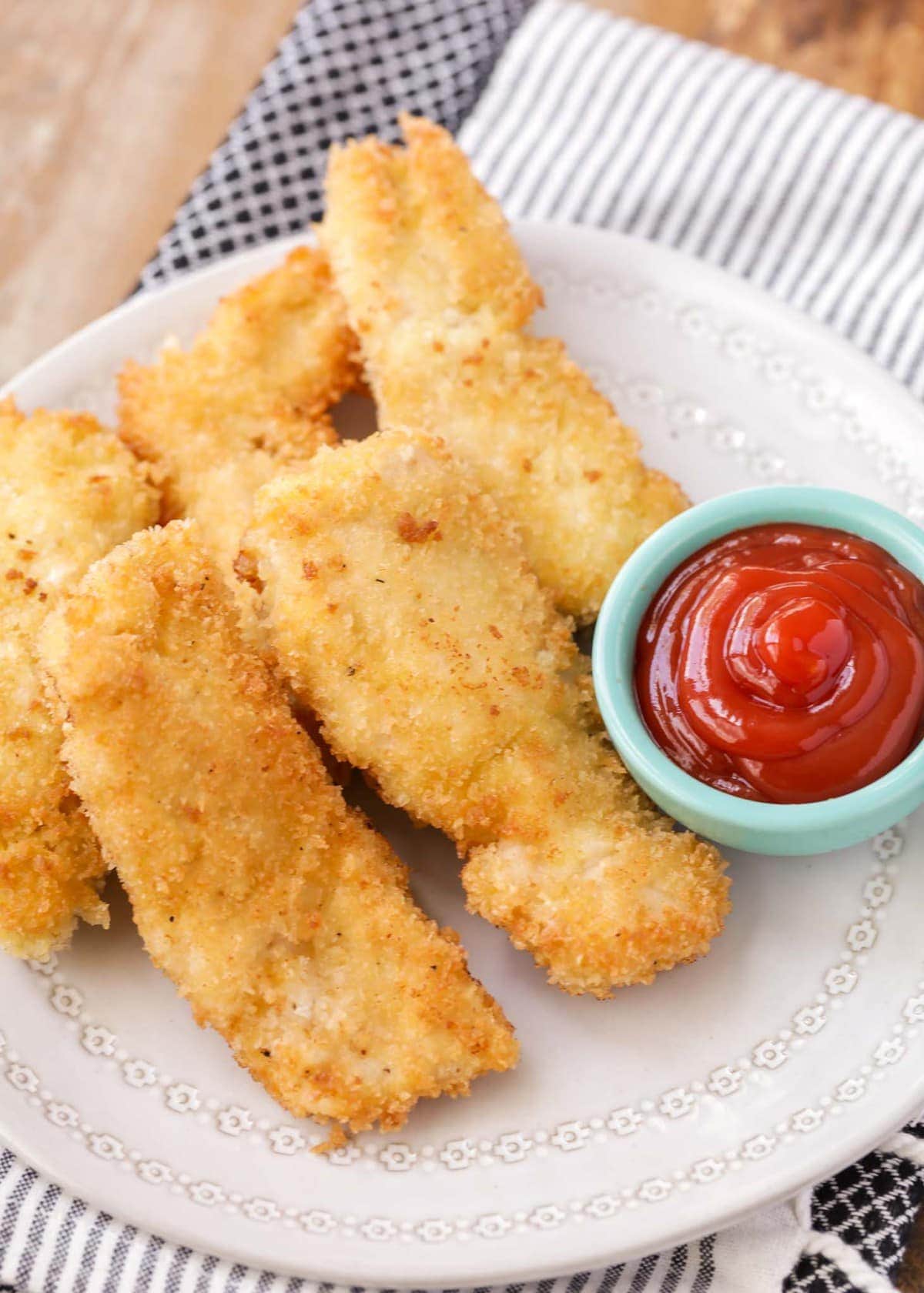Homemade chicken tenders on a plate with a side of ketchup