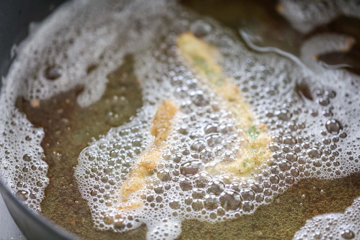 Deep fried green beans cooking in a skillet of oil.