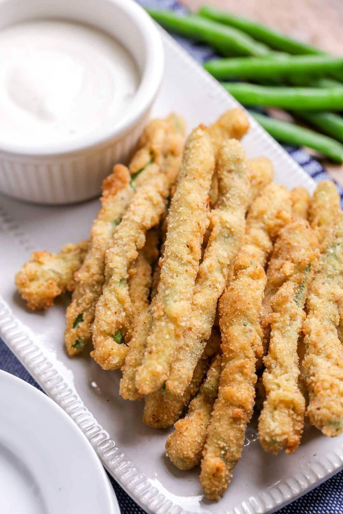 Green bean fries on a serving platter with a side of ranch dressing.