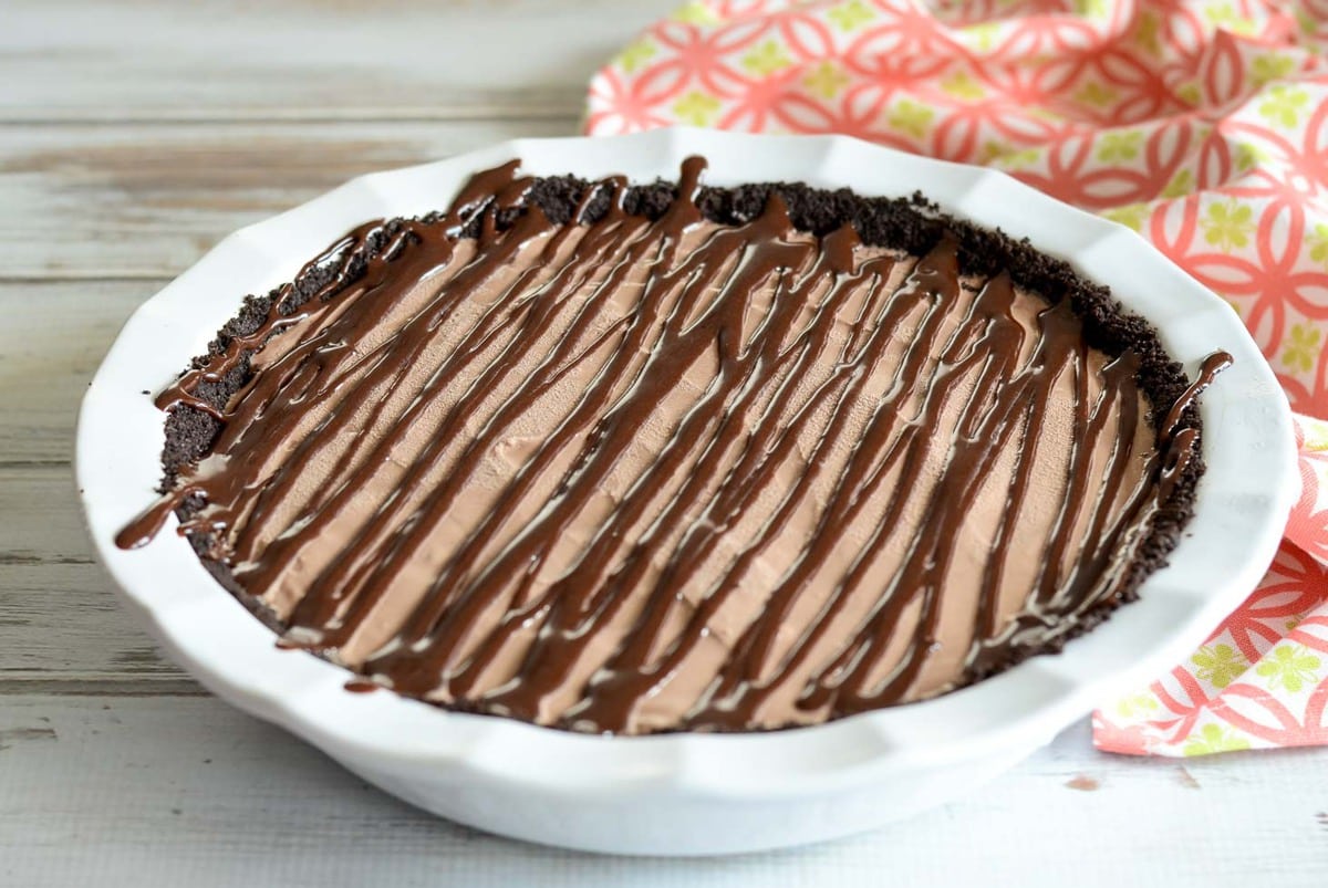 Mud pie drizzled with chocolate in a white pie dish.