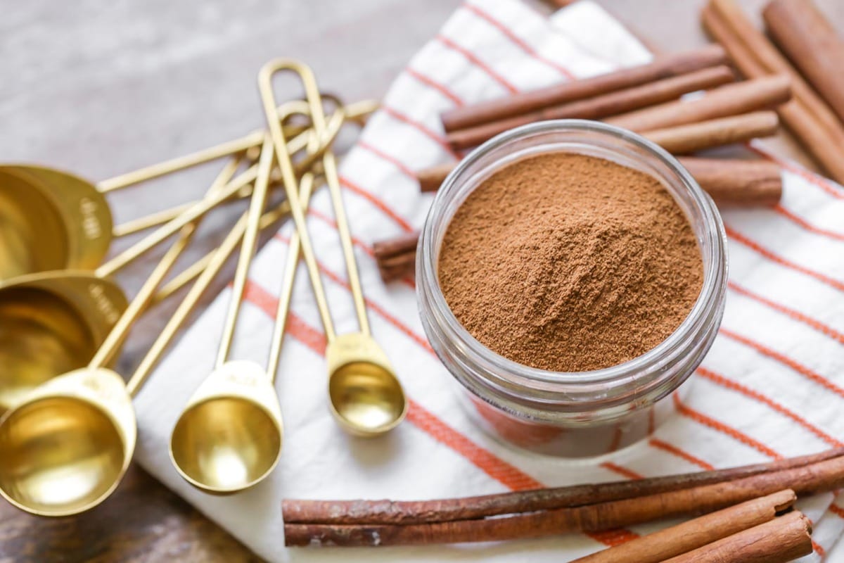 Pumpkin pie spice in a glass jar surrounded by cinnamon sticks.