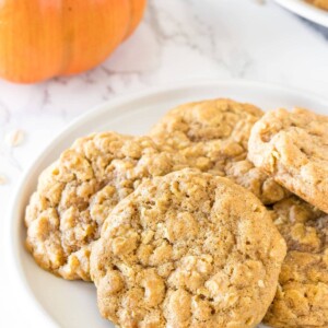 A plate of soft, oatmeal pumpkin cookeis with a mini pumpkin in the background.