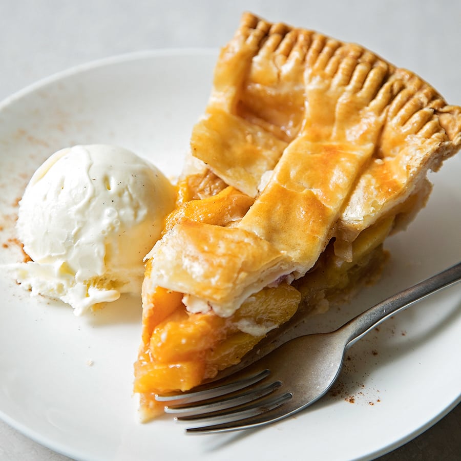 A slice of Peach Pie recipe on a plate with a scoop of vanilla ice cream.