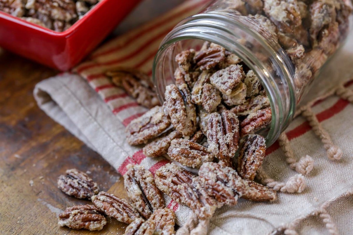 Candied pecans spilling out of a glass jar.