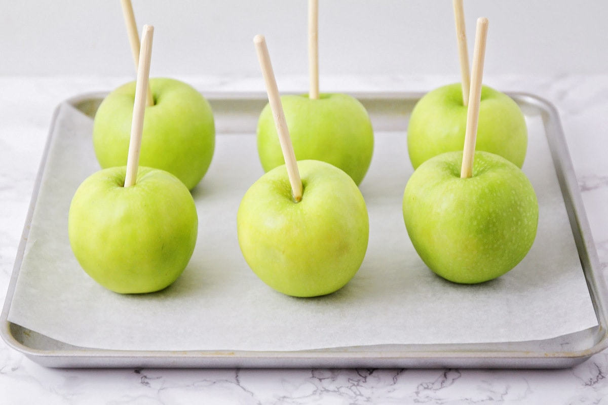 Granny smith apples stuck with wooden dowels on a lined baking sheet.