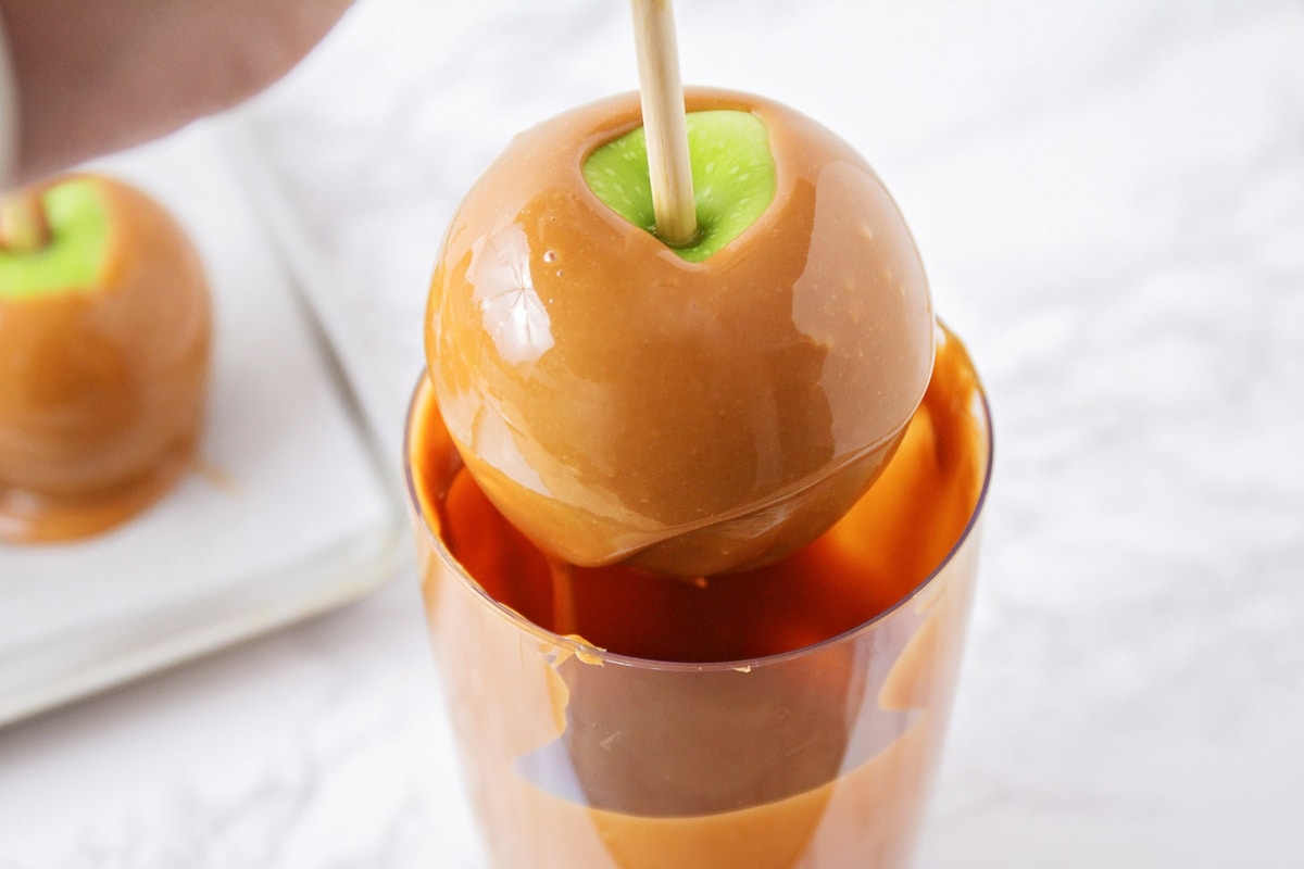 Dipping an apple into a cup of melted caramel.