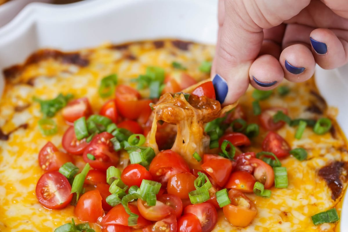 Appetizer Dips - Chili Cheese Dip in a white bowl topped with diced cherry tomatoes and chopped green onions.