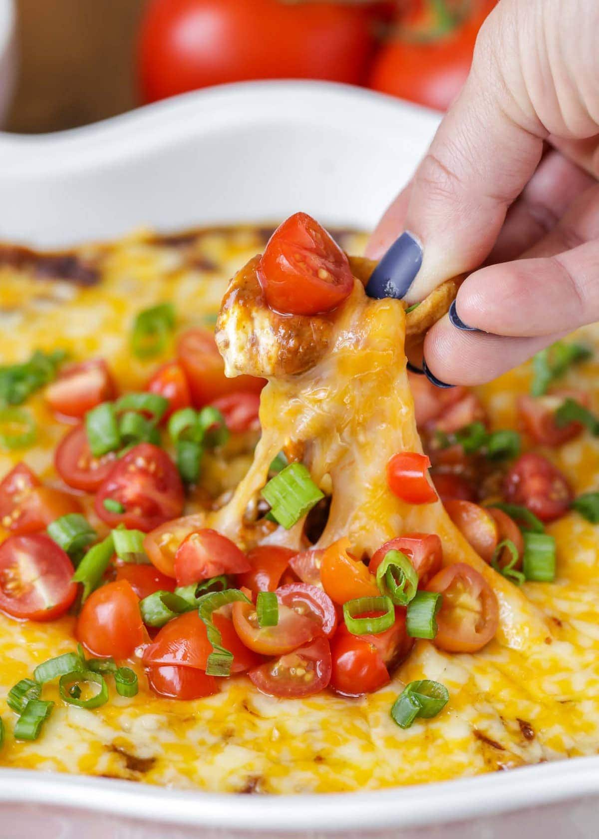 Close up of dipping a Frito chip into homemade chili cheese dip. 