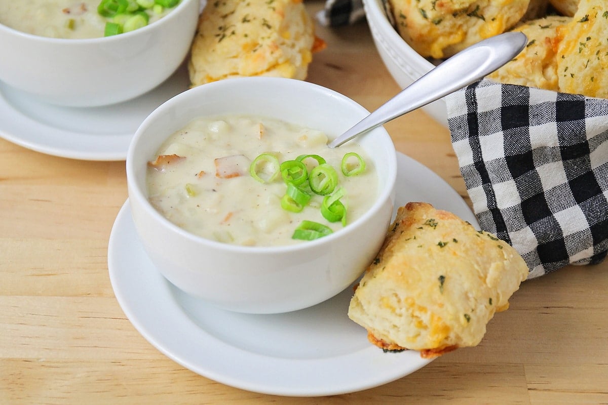 Clam chowder in a white bowl with biscuits on the side.