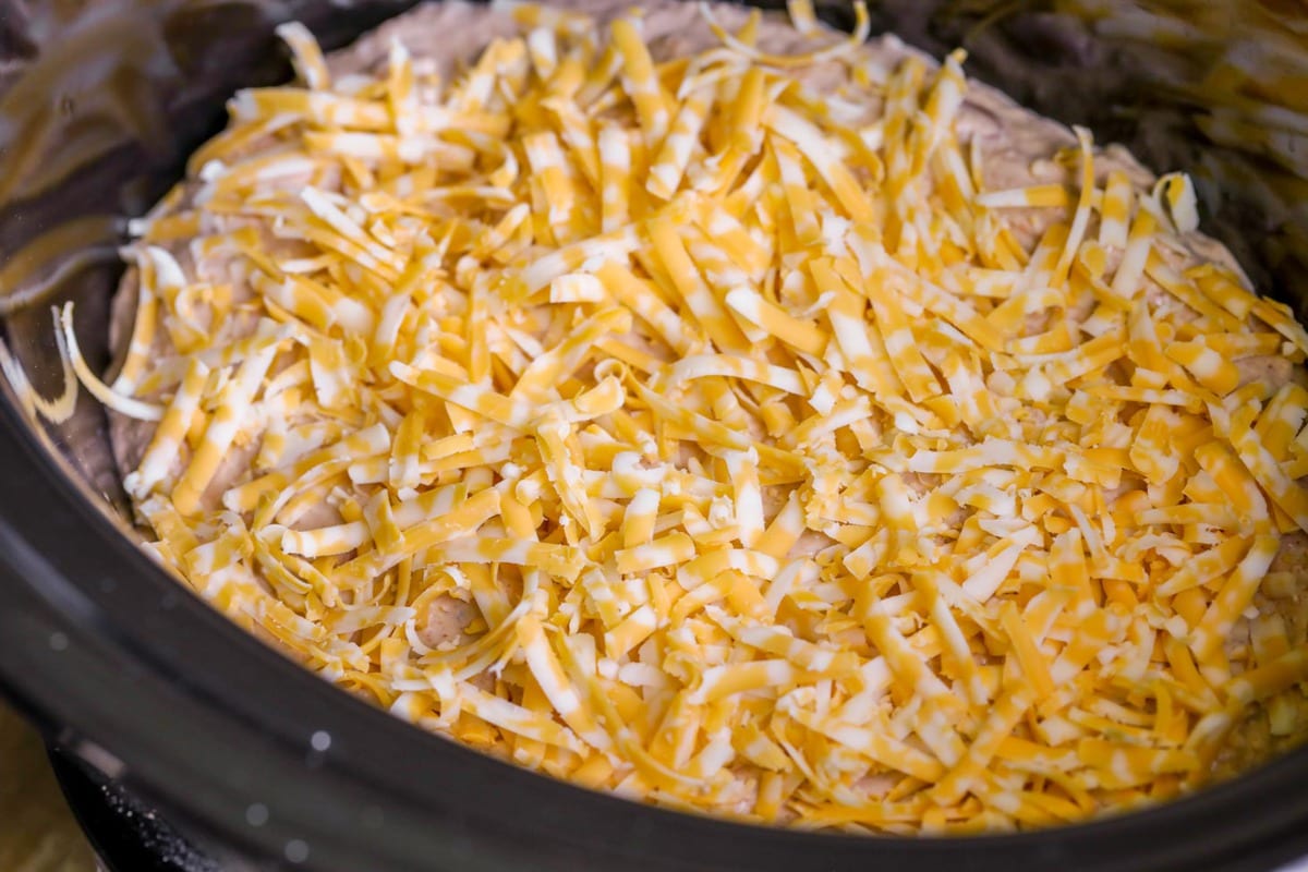 A slow cooker filled with bean dip topped with shredded cheese.