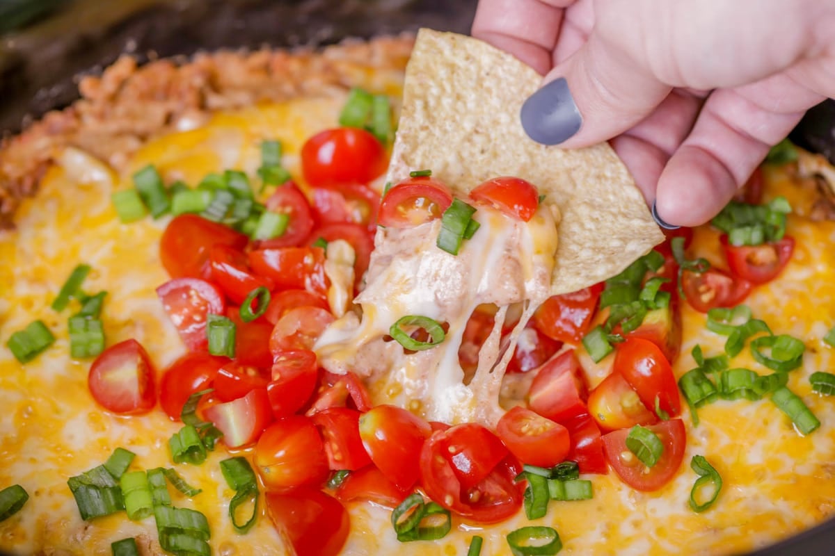 Crock Pot Appetizers - Crock Pot Bean Dip topped with melted cheese, diced green onions, and diced cherry tomatoes. 