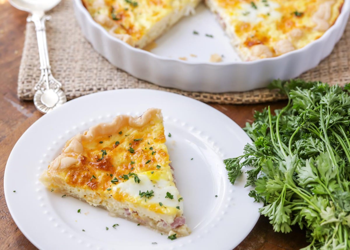 A slice of ham and cheese quiche on a white plate.