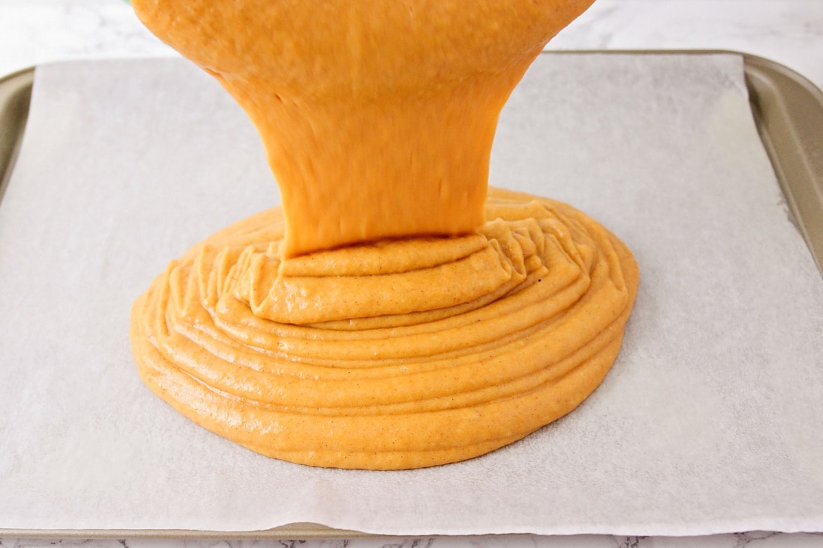 Pouring pumpkin bar batter onto a pan lined with parchment paper