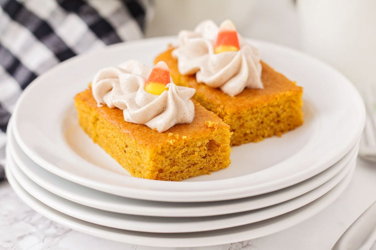 Dessert Bar Recipes - Pumpkin Bars topped with whipped cream and candy corns on a stack of white plates. 