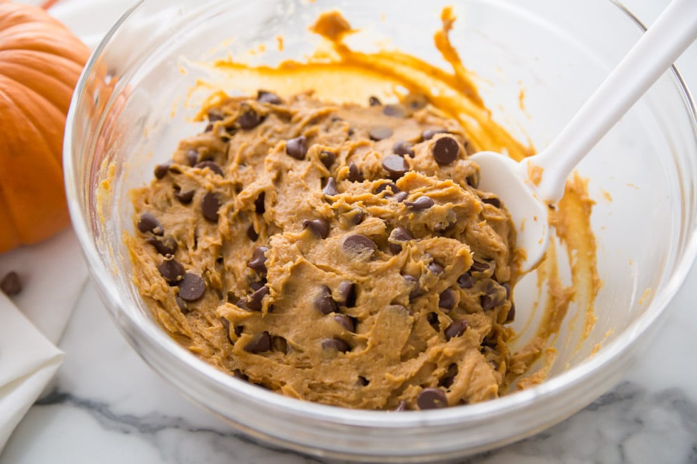 Mixing pumpkin cookie batter with chocolate chips in a bowl.