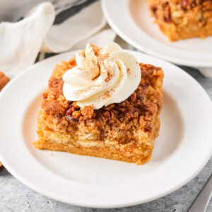 Pumpkin crunch cake slice on white plate with whipped cream on top.